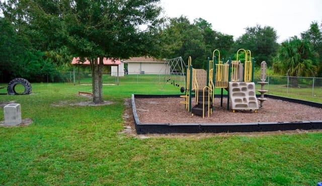 Playground equipment at Joe Culliver Park in LaBelle, Florida, surrounded by green grass and trees.